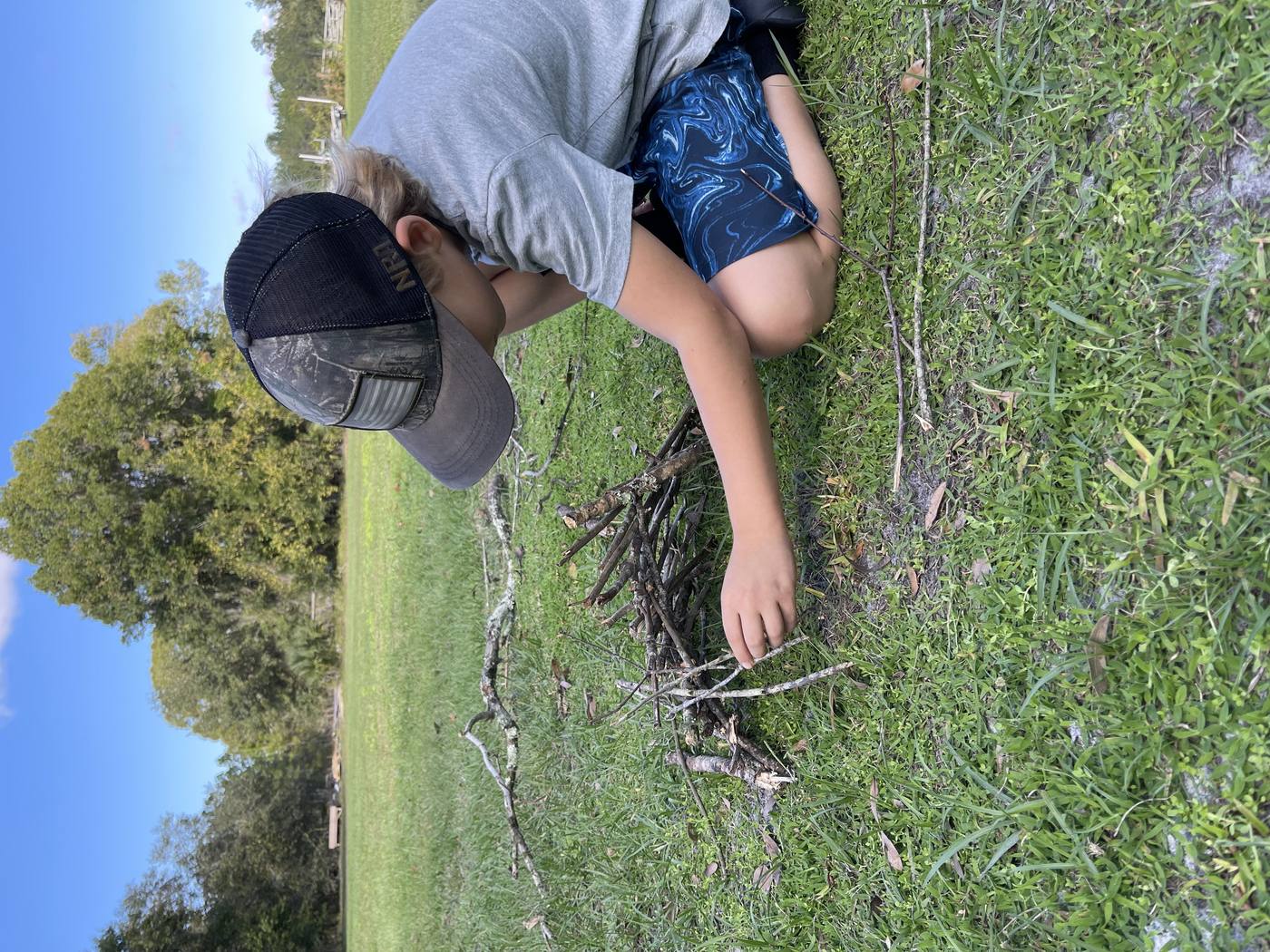 Young student building a small structure from sticks in a grassy field during outdoor learning